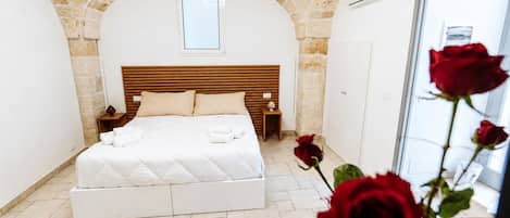 Un dormitorio con techo abovedado de piedra, cabecero de madera, cama con ropa de cama blanca, mesita de noche y una ventana.