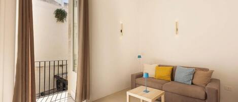 A living room with a sofa, a small table, and a balcony with curtains.