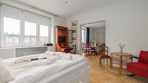 Un dormitorio con cama, televisor, aparador de madera, mesa de comedor con sillas y una butaca roja.