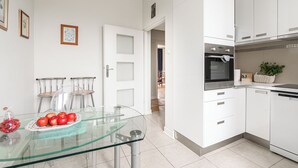Una cocina moderna con armarios blancos, una mesa de vidrio con sillas y una planta en la encimera.