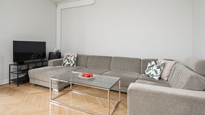 Una sala moderna con un sofá gris, una mesa de centro de vidrio y un televisor de pantalla plana sobre un soporte negro.