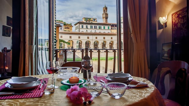 Mesa posta com pratos, copos e uma vela, com vista para um edifício histórico com torre.