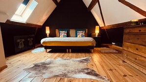 A bedroom with a sloped ceiling, wooden flooring, a bed with colorful pillows, a fur rug, and a dresser. - Gîte Origin route des vins d'Alsace (Gueberschwihr)