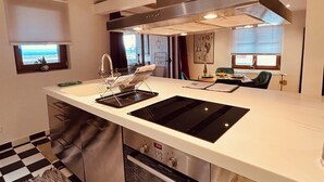 A modern kitchen with a central island, stainless steel appliances, and a checkered floor. - Gîte Origin route des vins d'Alsace (Gueberschwihr)