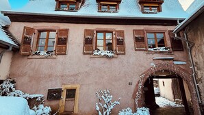 A traditional building with multiple windows, a wooden door, and a snow-covered entrance. - Gîte Origin route des vins d'Alsace (Gueberschwihr)