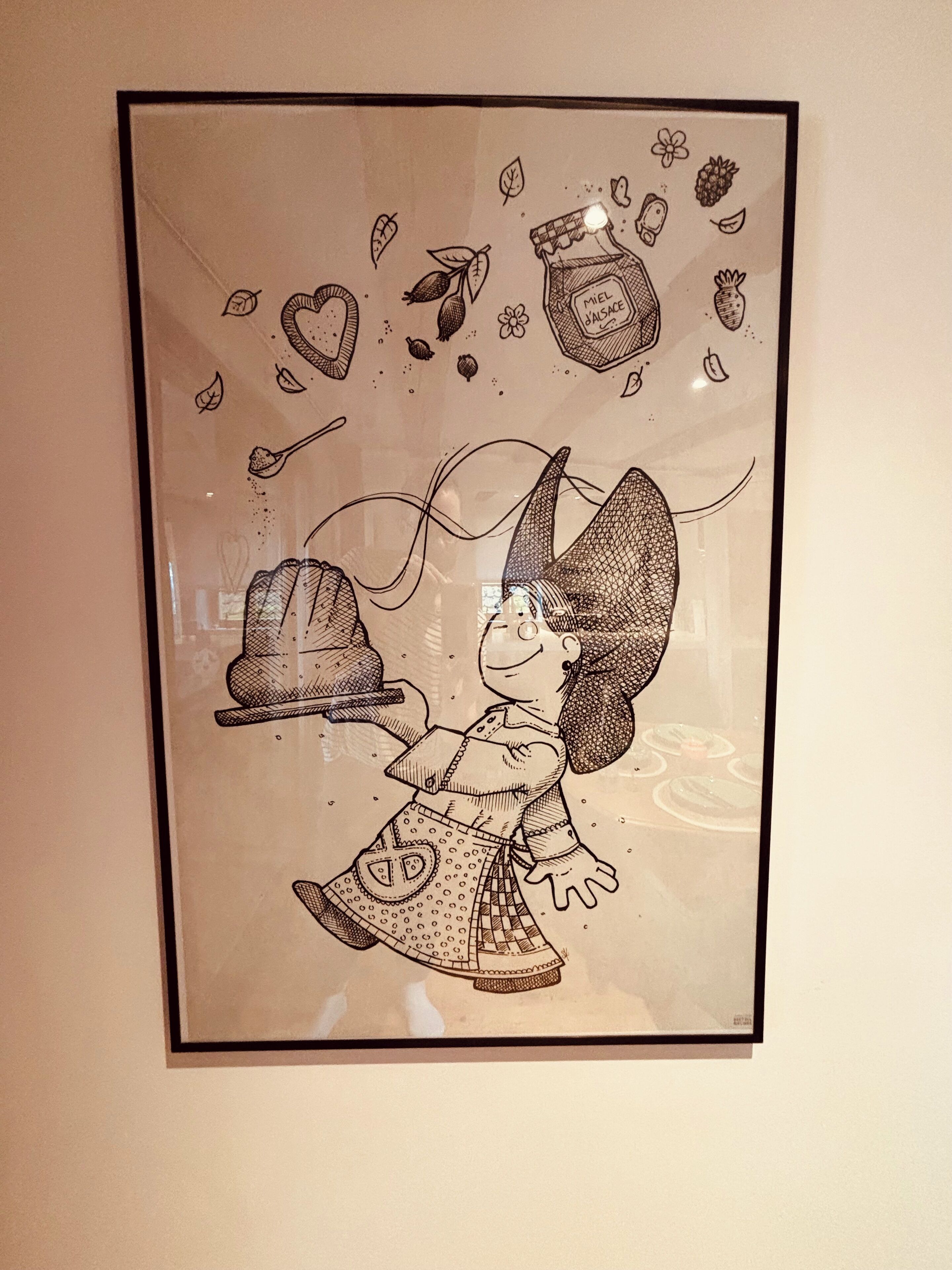 Une illustration encadrée représentant un personnage fantaisiste tenant un chapeau, entouré d’objets flottants tels que des feuilles et une bouteille.