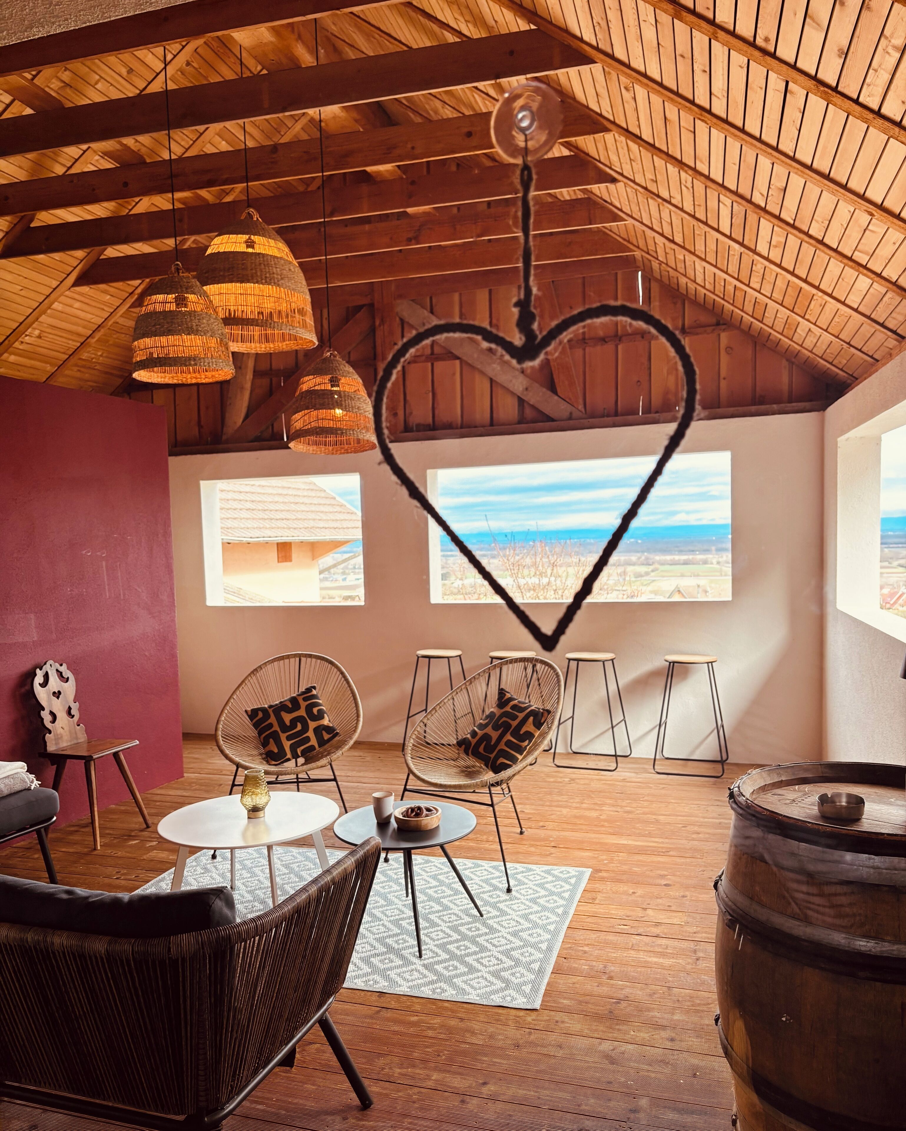 A cozy room with wicker furniture, a heart-shaped decoration, and large windows offering a view of the beach.