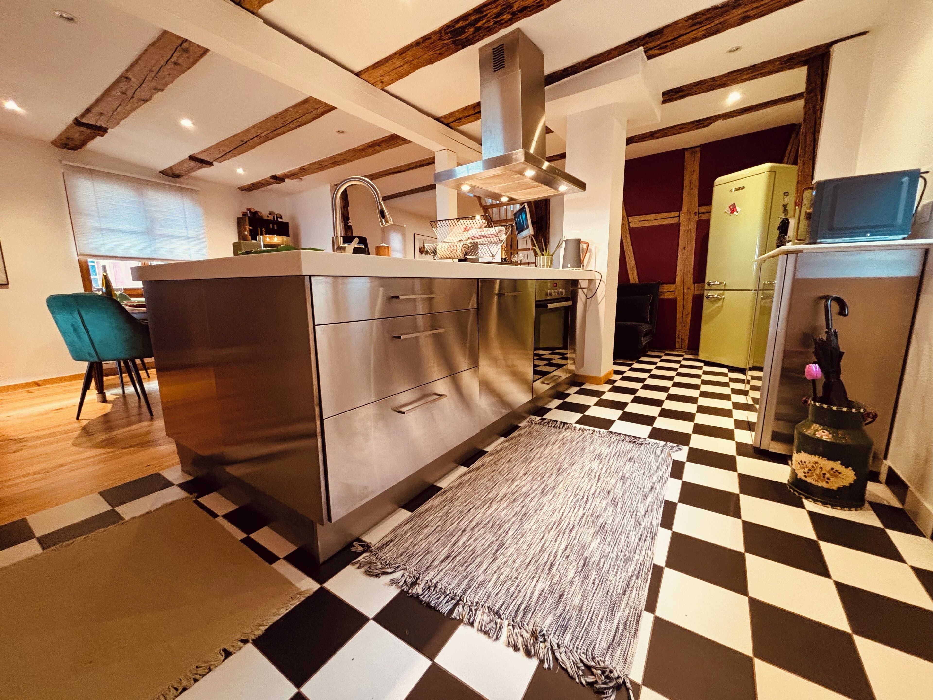 Une cuisine moderne avec un carrelage à motifs, des appareils électroménagers en acier inoxydable et des poutres en bois au plafond.