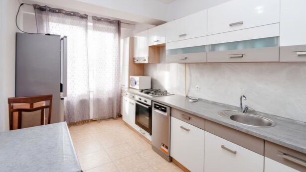 Une cuisine moderne avec des meubles blancs, une cuisinière, un évier et un coin repas comprenant une table et des chaises.
