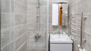 Une salle de bain moderne avec une douche à parois de verre, un lavabo blanc et un miroir doté d’un porte-serviettes.