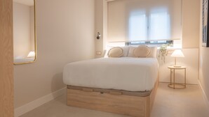 Un dormitorio con cama, mesita de noche, lámpara, espejo y ventana con persianas.