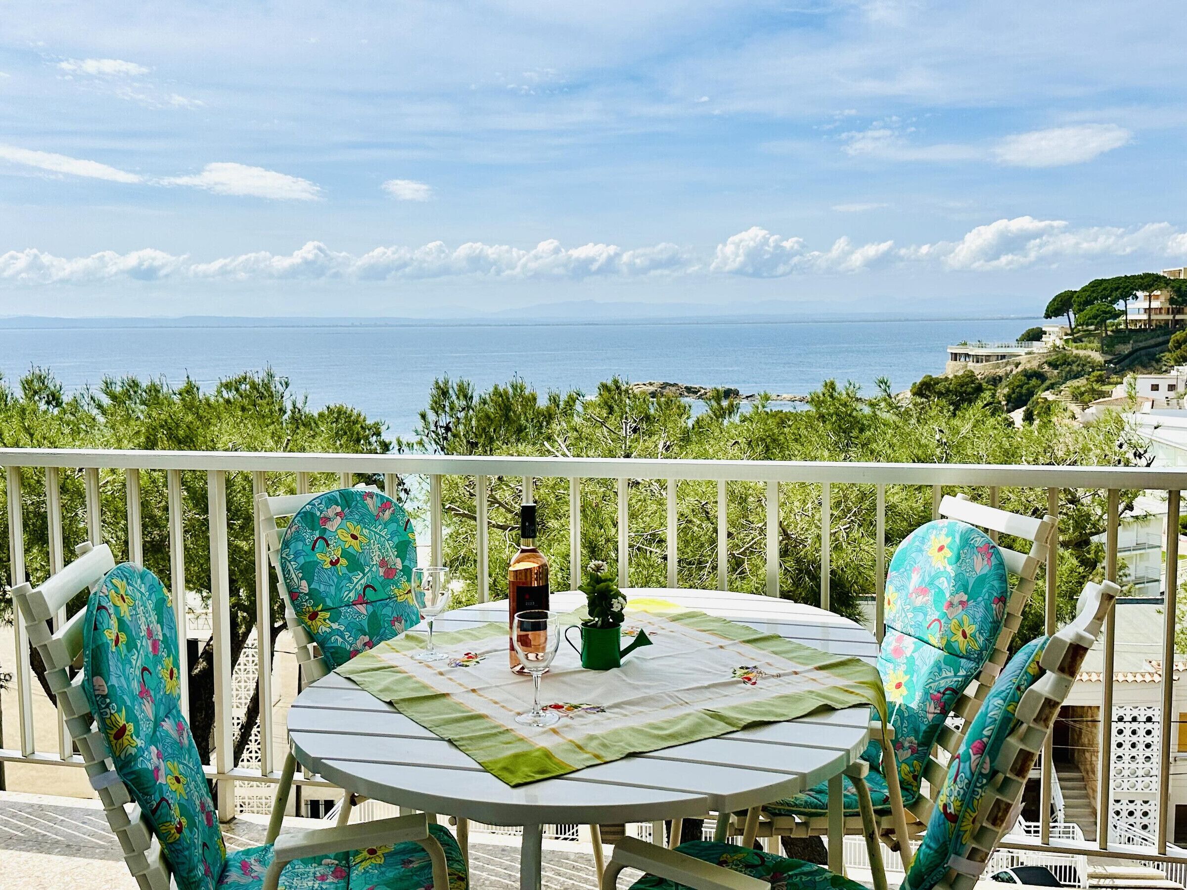 A round table with chairs, a bottle, and a glass on a balcony overlooking the sea.