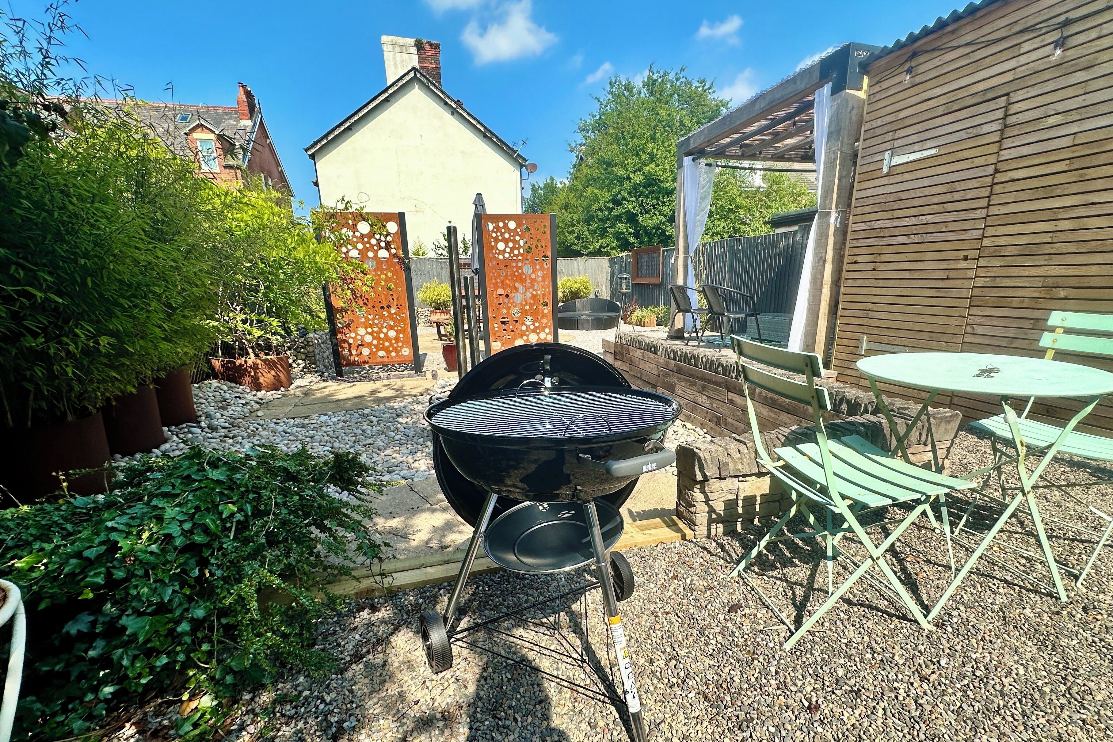 En trädgård med en grillplats, utomhusmöbler och en trädgårdsdel.