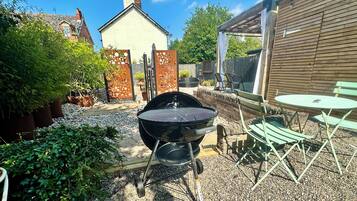 En trädgård med en grillplats, utomhusmöbler och en trädgårdsdel.