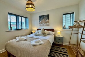 A bedroom with a bed, bedside lamps, a painting, a window, and a wooden ladder.