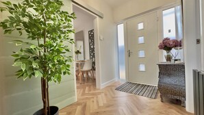 Ein Flur mit Zimmerpflanze, einer Tür mit Fenster, einem Heizkörper und einem kleinen Tisch mit Blumenvase.