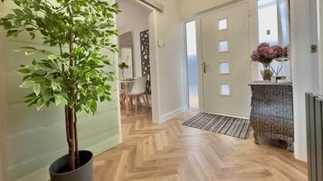 En hall med en krukväxt, en dörr med ett fönster, ett element och ett litet bord med en vas med blommor.