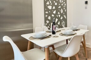 A dining table set with white plates, glasses, and a bottle, surrounded by white chairs.