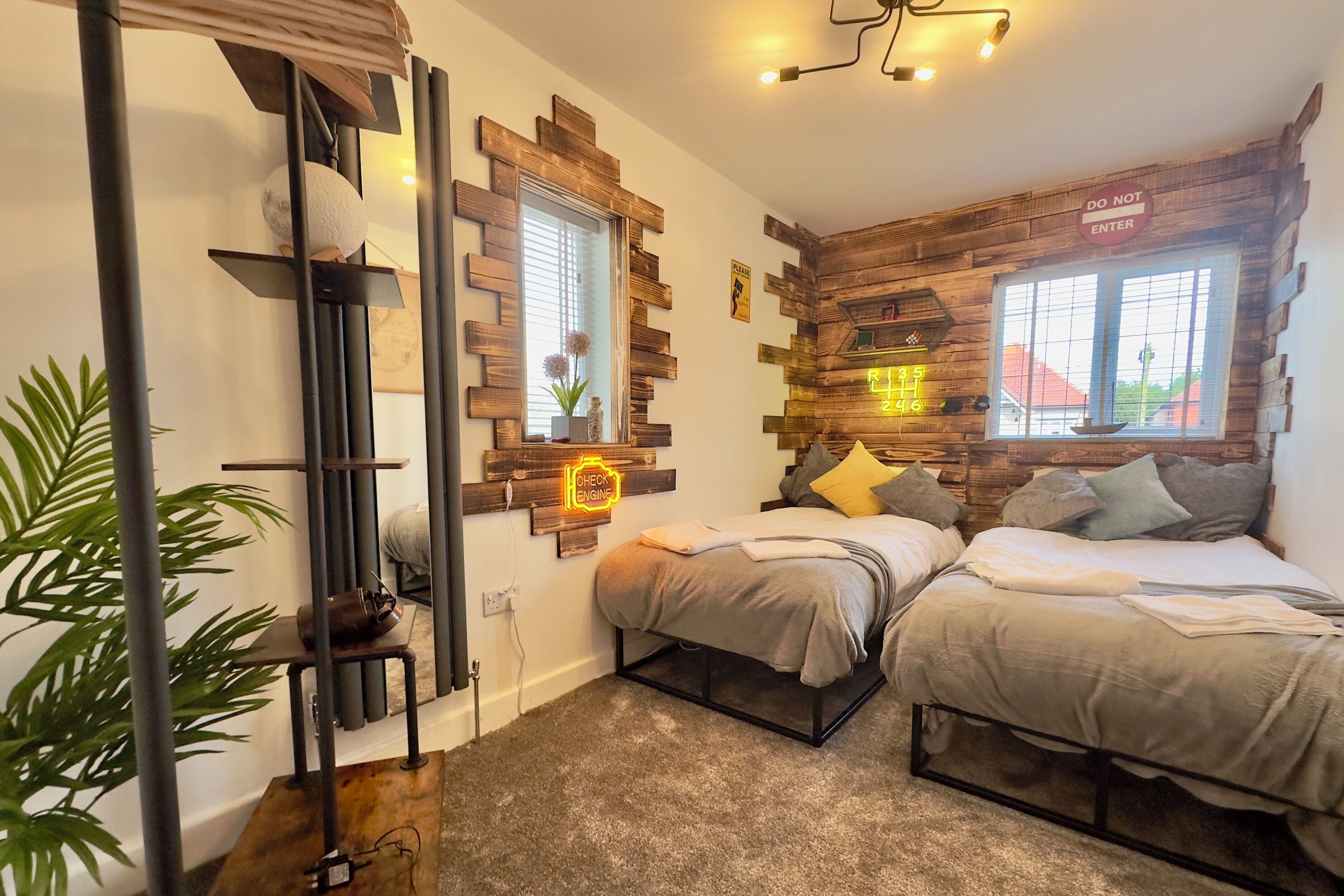 A room with two beds, a wooden accent wall, a check engine sign, and a plant.