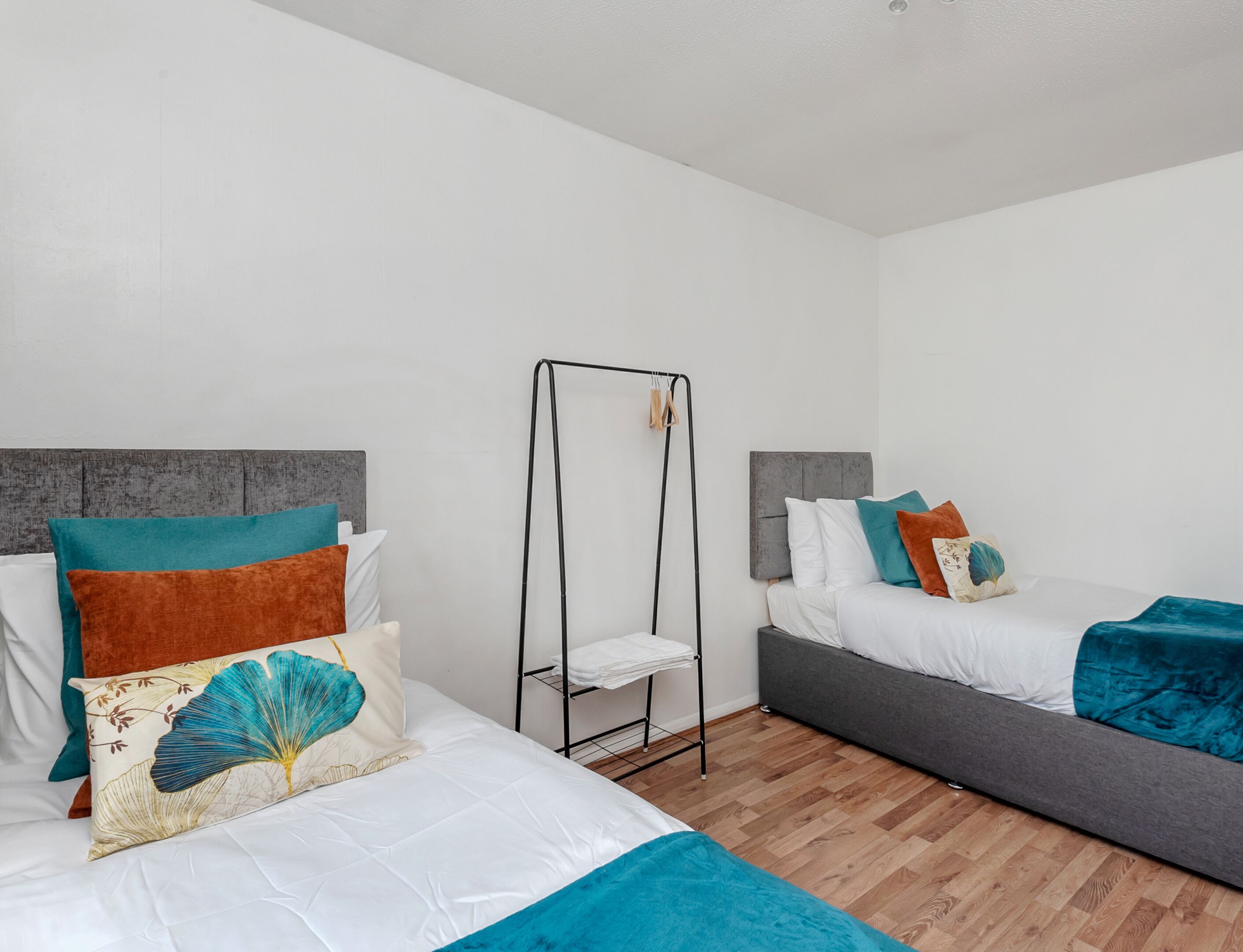 A hotel room with two beds, a metal drying rack, and wooden flooring.