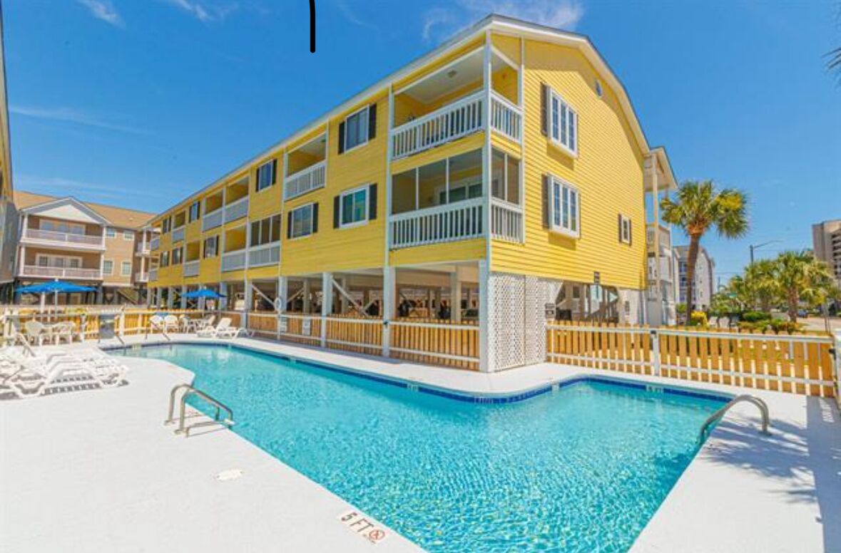 A yellow building with balconies and a swimming pool.