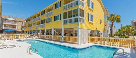 A yellow building with balconies and a swimming pool.