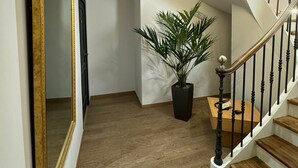 Portaat, joissa on puiset askelmat ja mustat kaiteet, suuri peili kultaisella kehyksellä sekä ruukkuun istutettu kasvi käytävällä.