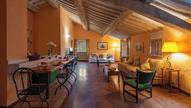 A spacious living area with a high ceiling, a dining table, chairs, a sofa, and a lamp. - La Foresteria Castell'In Villa (Castelnuovo Berardenga)