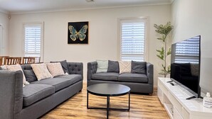 A modern living room with two grey sofas, a round coffee table, and a flat-screen TV on a white stand. - Family and Group Holiday Home Sleeps 13 Near Western Sydney Airport, Penrith (Jordan Springs)