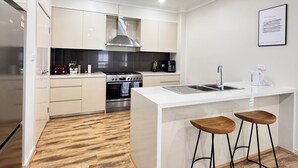 A modern kitchen with white cabinetry, a stainless steel range hood, a built-in oven, a double sink, and two wooden bar stools. - Family and Group Holiday Home Sleeps 13 Near Western Sydney Airport, Penrith (Jordan Springs)