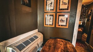 Una habitación con una mesa de madera, aire acondicionado de pared y cuadros con pájaros en la pared.