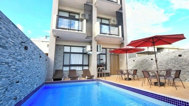 A modern hotel with a swimming pool, outdoor seating, and a stone wall. - New One Villa (Hengchun)