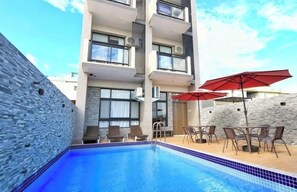 A modern hotel with a swimming pool, outdoor seating, and a stone wall.