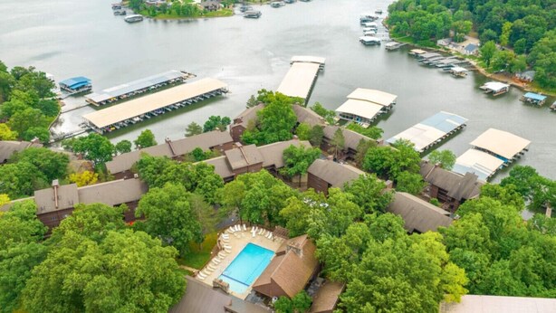A lakeside property with multiple docked boats, a swimming pool, and lush greenery.