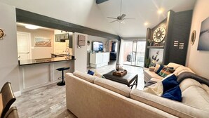 A spacious living area with a large sofa, a coffee table, and a dining area with a kitchen in the background.