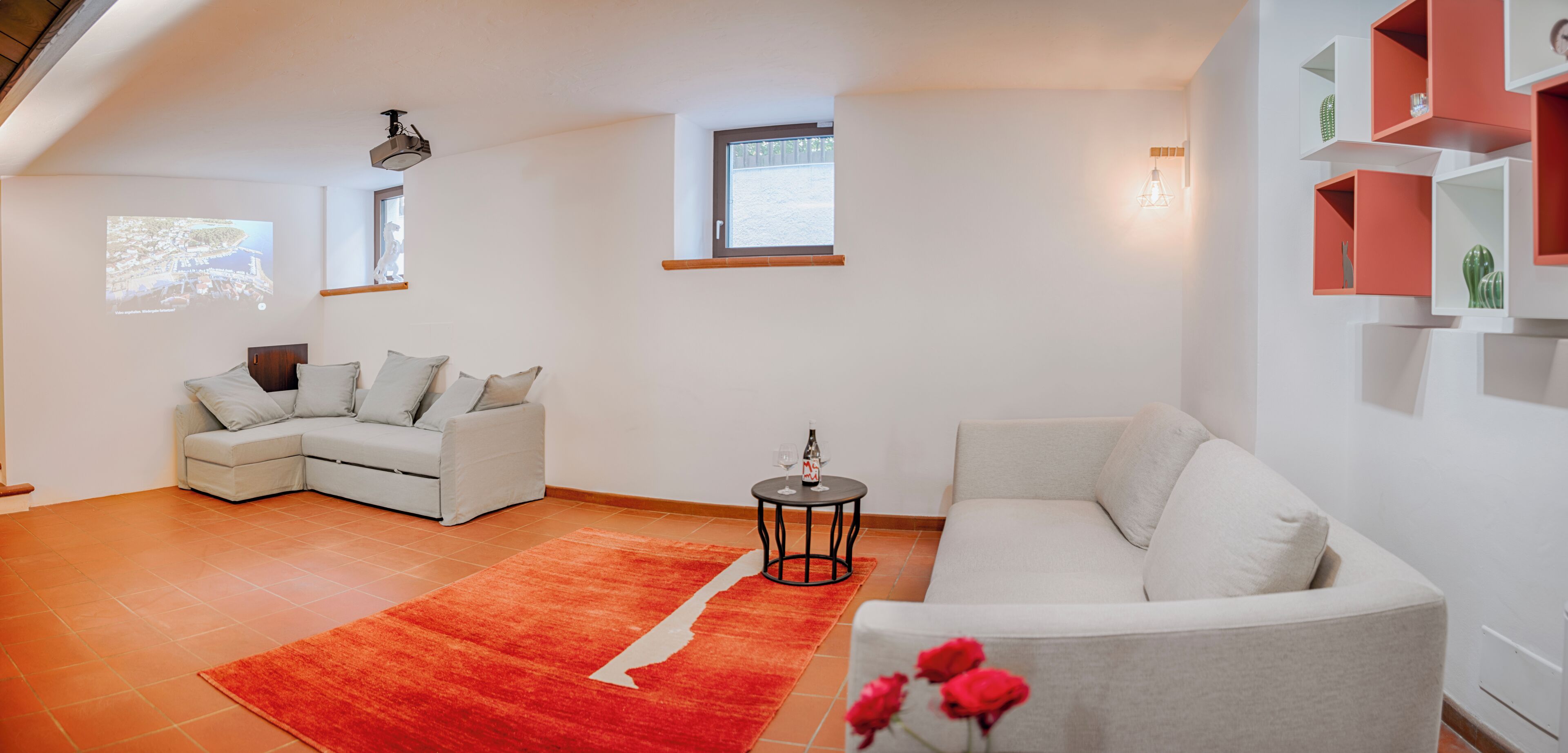 Una sala de estar moderna con un sofá blanco, un tapete rojo y una pequeña mesa con una botella.