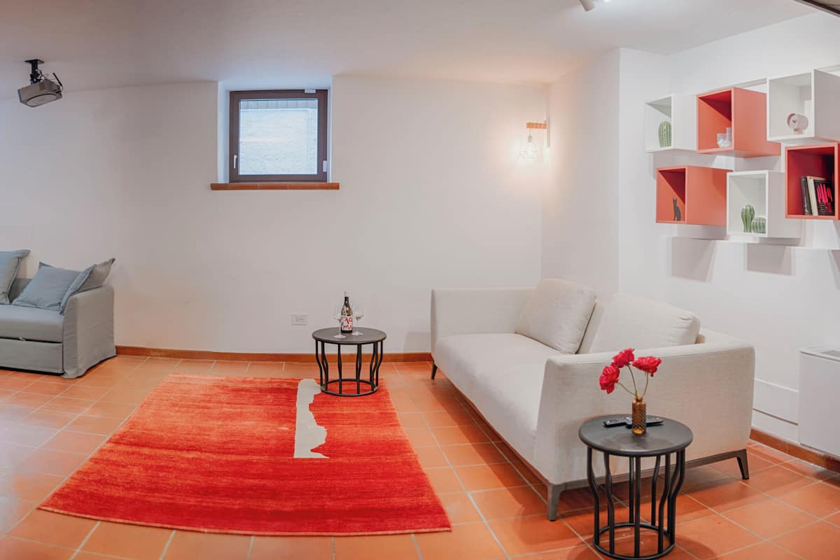 A living room with a grey sectional sofa, a white sofa, a red rug, and a wall with shelves.