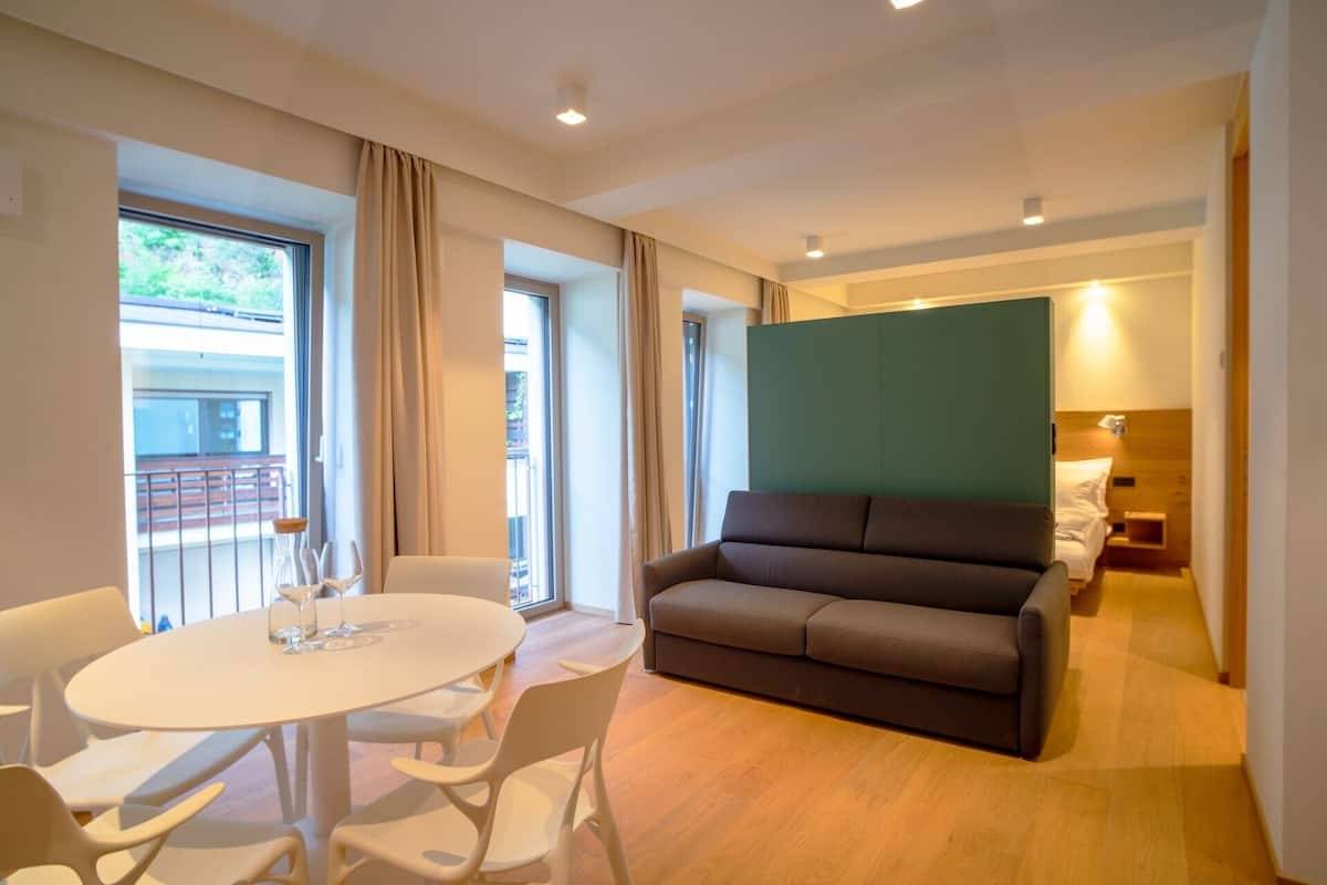 A modern hotel room with a round dining table, a sofa, and a balcony with a railing.