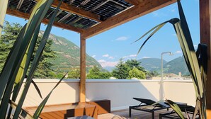 Terraza en la azotea con suelo de madera, una mesa, dos sillas y una pérgola con paneles solares.