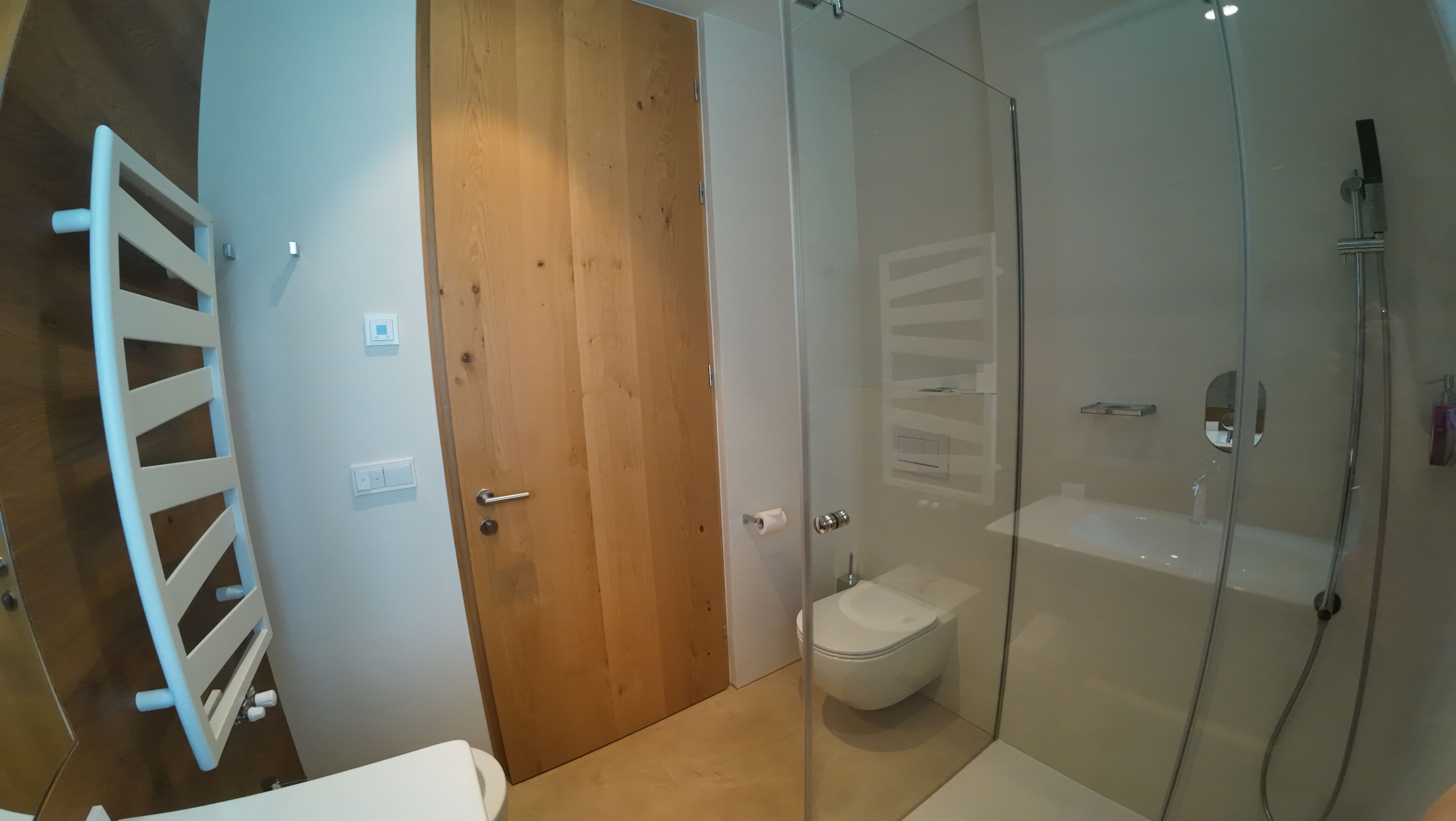 Een badkamer met een douchecabine van glas, een houten deur en een wit toilet.