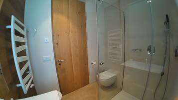 Een badkamer met een douchecabine van glas, een houten deur en een wit toilet.