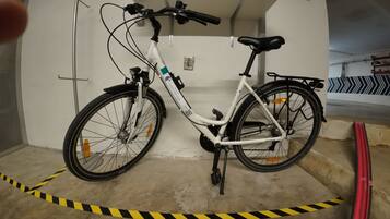 Un vélo blanc avec une selle et un guidon noirs, garé dans un garage où du ruban de signalisation jaune et noir est disposé sur le sol.