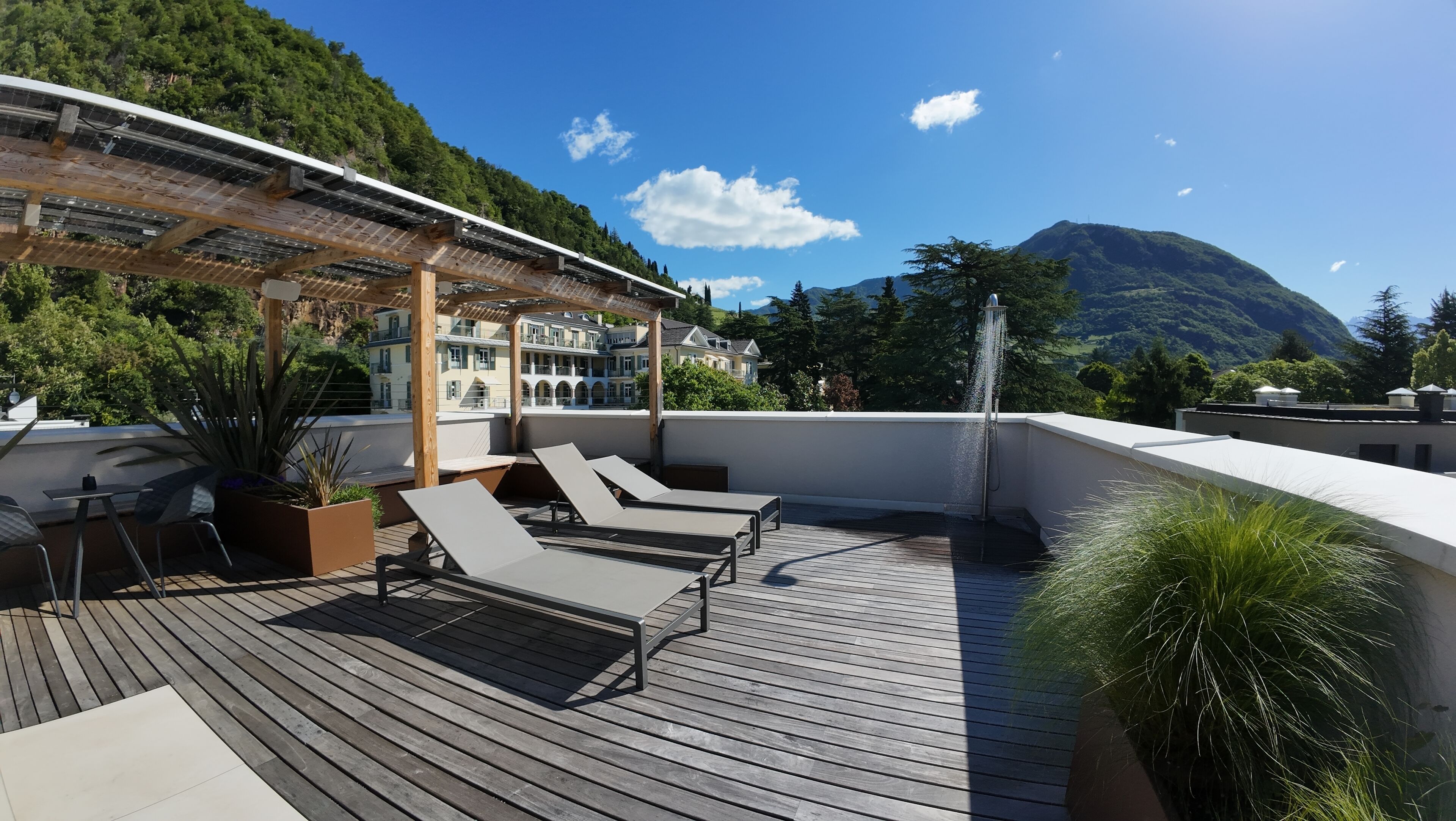 Una terrazza sul tetto con poltrone relax, un pergolato e vista su una montagna.