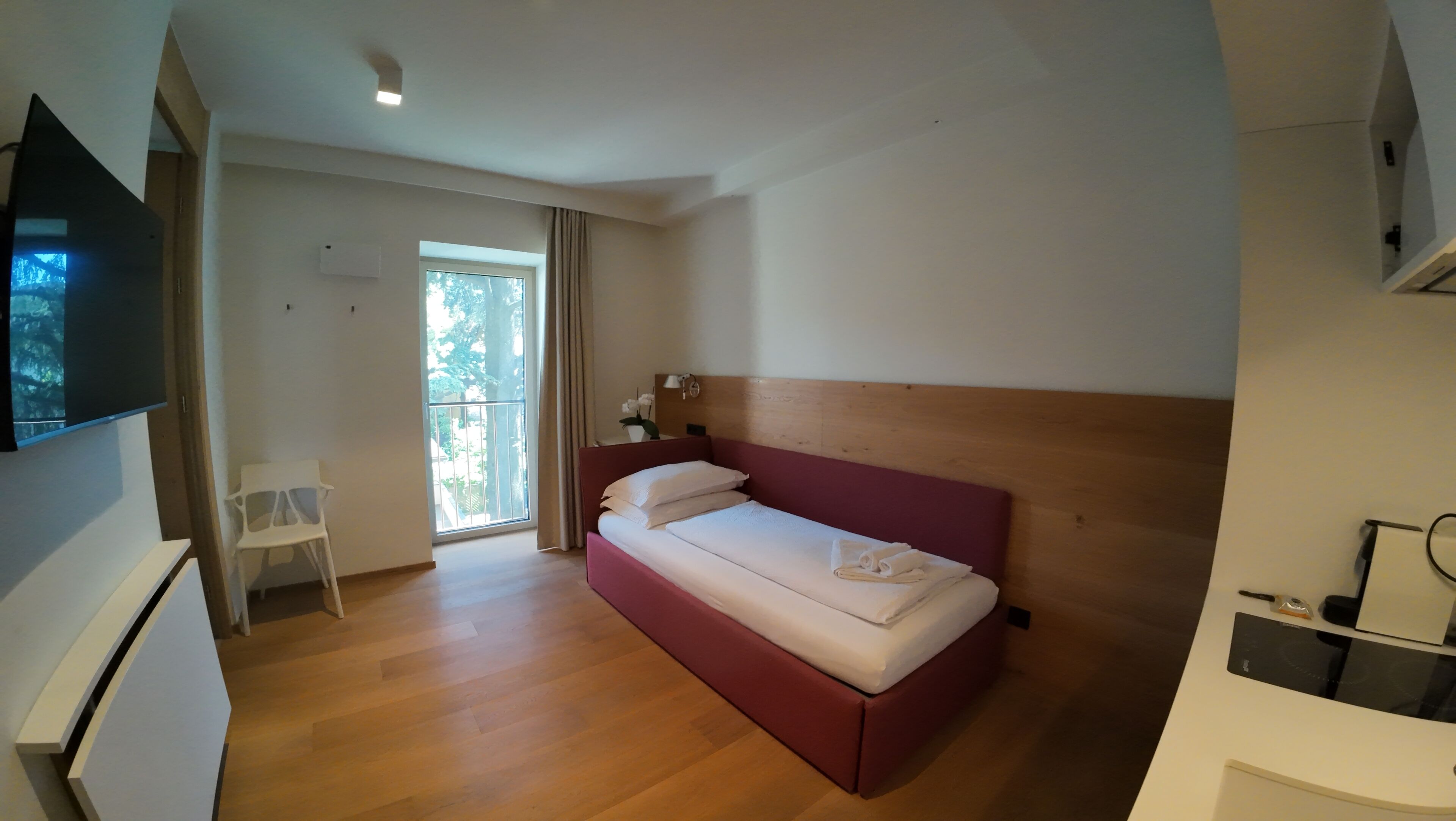Una camera da letto con un letto, una scrivania, una sedia, una TV e una finestra con tende.