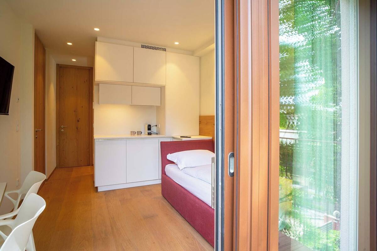 A compact room with a bed, kitchenette, and a sliding door to a balcony.