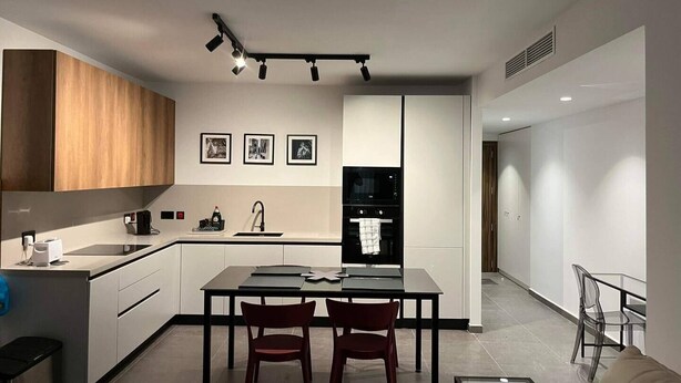 A modern kitchen with a dining area, featuring a central island, wooden cabinets, and a black refrigerator. - Centrally located in Qawra, this modern 2-bed apartment offers comfort, style & easy access to the promenade — perfect for a carefree holiday escape! (San Pawl il-Baħar)