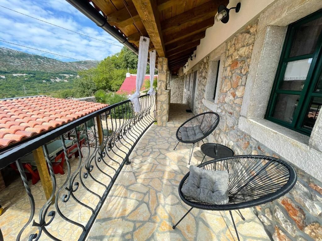 A balcony with stone flooring, two black chairs with cushions, and a red-tiled roof.