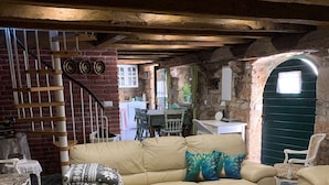 A cozy living room with a beige sofa, a wooden coffee table, and a wicker ottoman. A staircase with a metal railing and a brick wall is visible in the background. - Villa Paun (Vinodol)