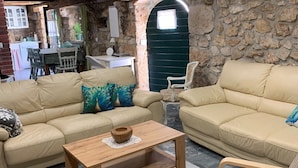 A cozy living room with two beige sofas, a wooden coffee table, and a wicker ottoman. A stone wall and a wooden door with a window are visible in the background. - Villa Paun (Vinodol)