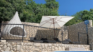 A pool area with stone walls, lounge chairs, and a large umbrella. - Villa Paun (Vinodol)